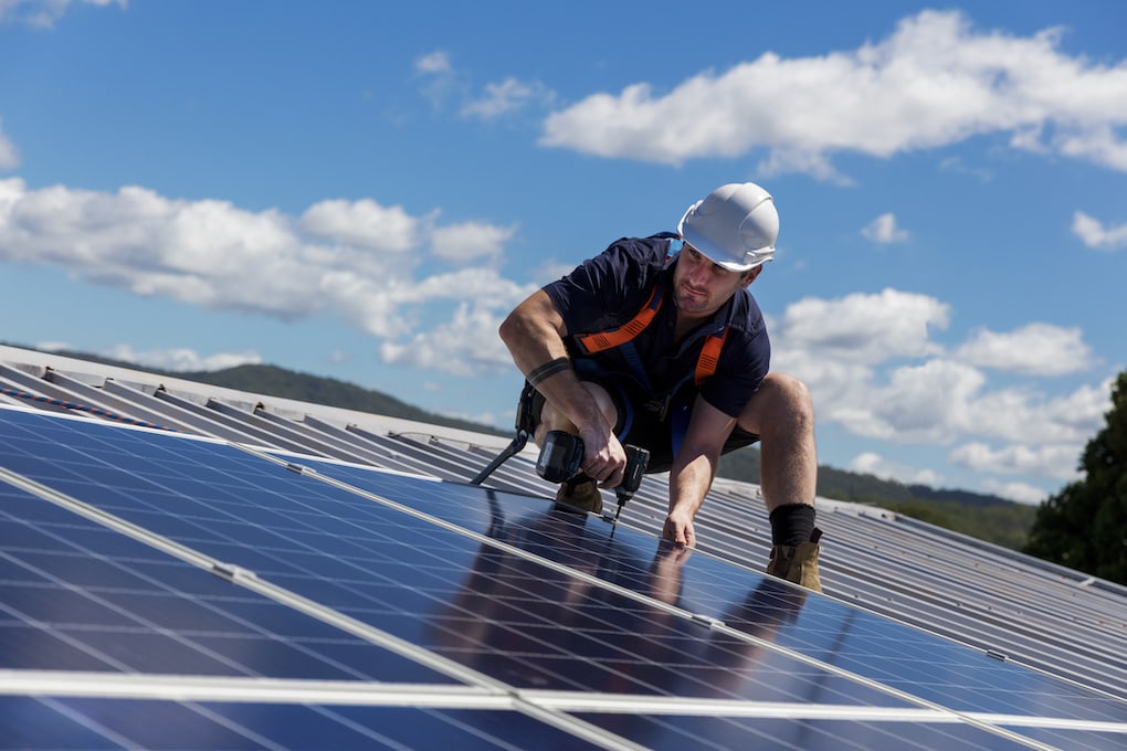 roof worker in white hard hat installing blue solar panels