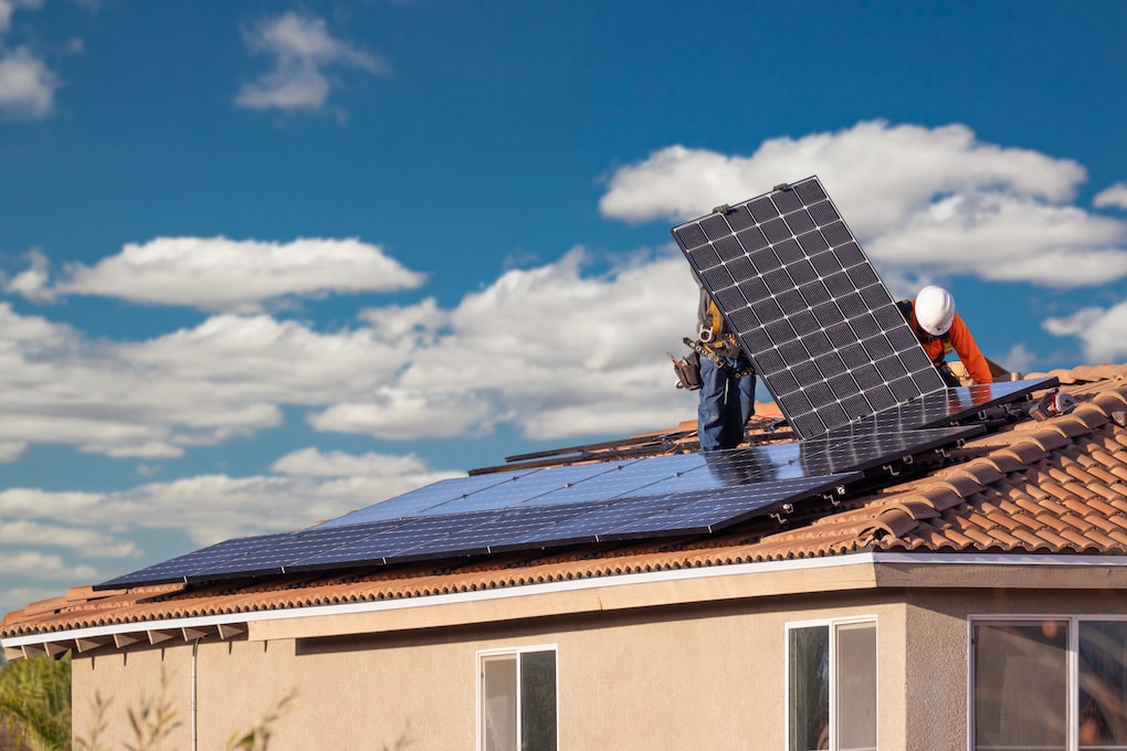 two roof workers laying a solar panel on a metal tile roof in florida