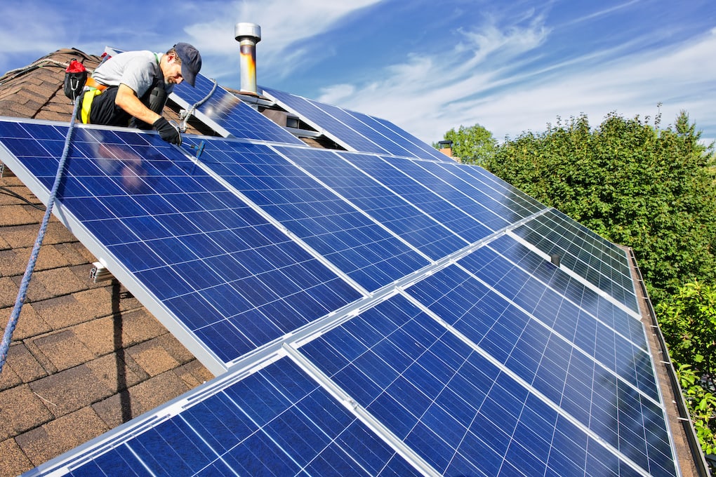 roof workers installing blue solar panels on a shingle roof