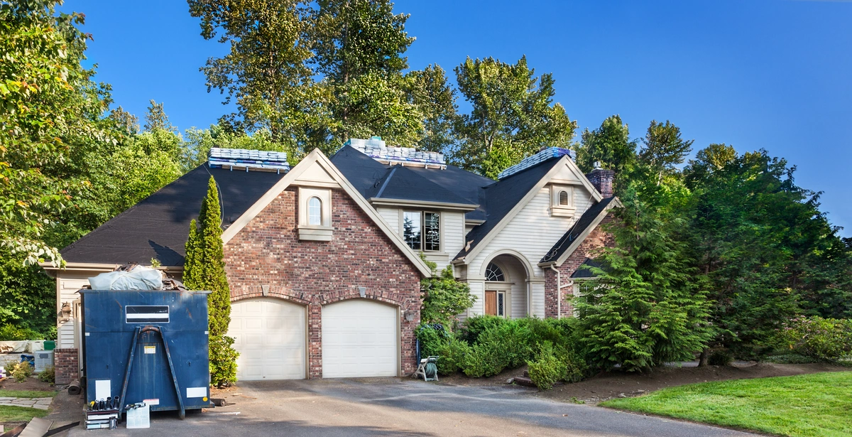 brick home with roof being replaced and construction materials on the driveway