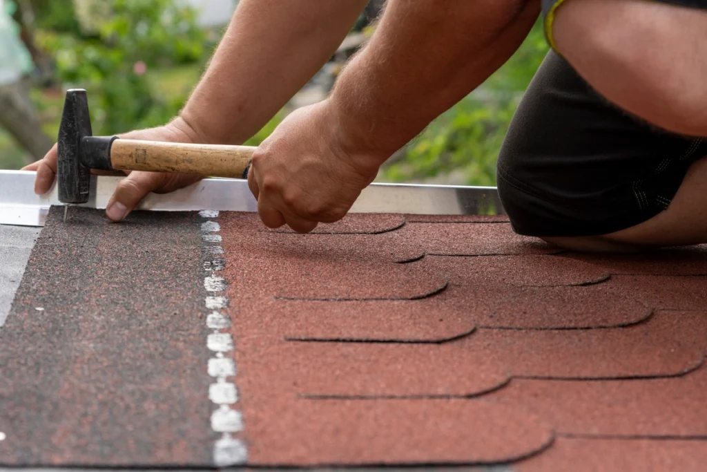 man using hand tools to install shingles on a roof