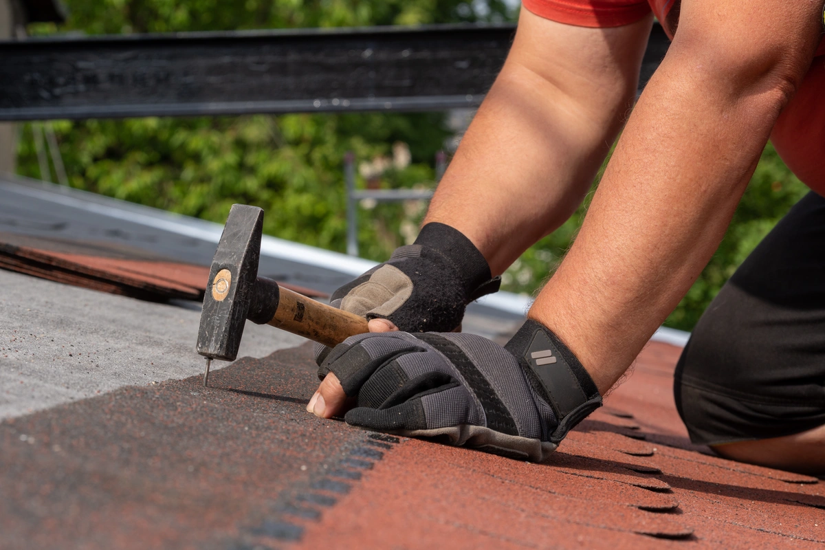 man wearing safety gloves using hand tools to install shingles on a roof