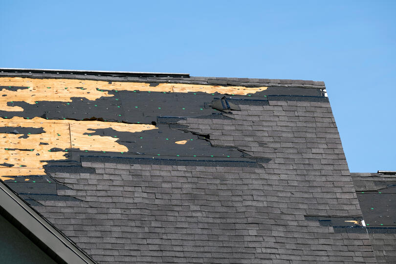 missing shingles-large portion of dark gray shingled roof is missing shingles and other roofing materials