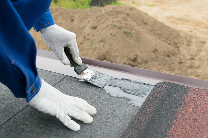 roof sealant-tech using a palette knife to apply a sealant to shingle roofing material