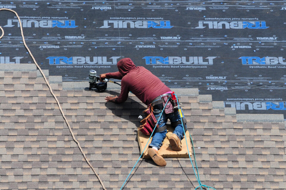 roofing tools-roofer wearing safety harness and using power tools to install shingles on a roof