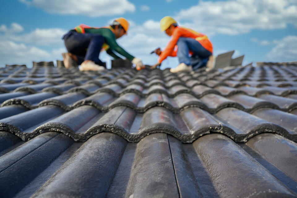 roofing tools-two roofers wearing safety gear installing concrete tile shingles on a roof